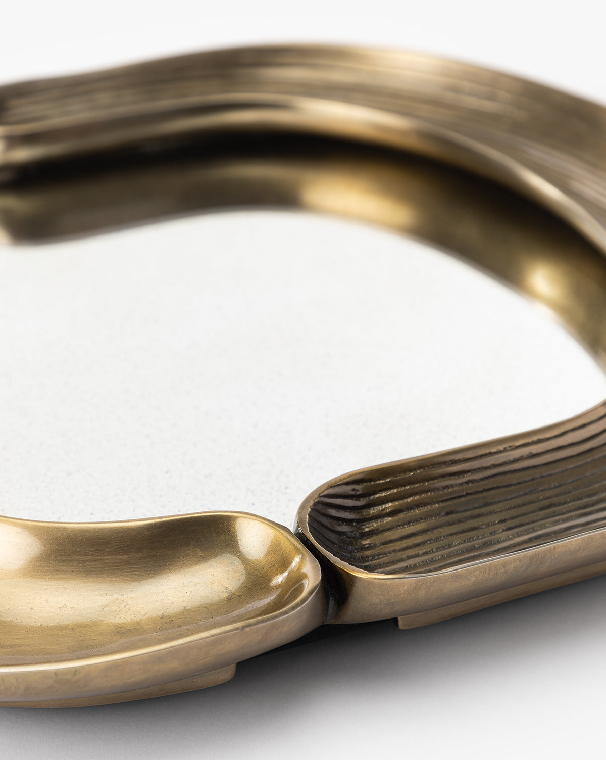 A close-up of the Salvatore Wall Mirror, featuring curved, textured brass sections and a smooth white center. Its artistic, modern design showcases an antique gold finish with a mix of matte and shiny surfaces by Vendixs