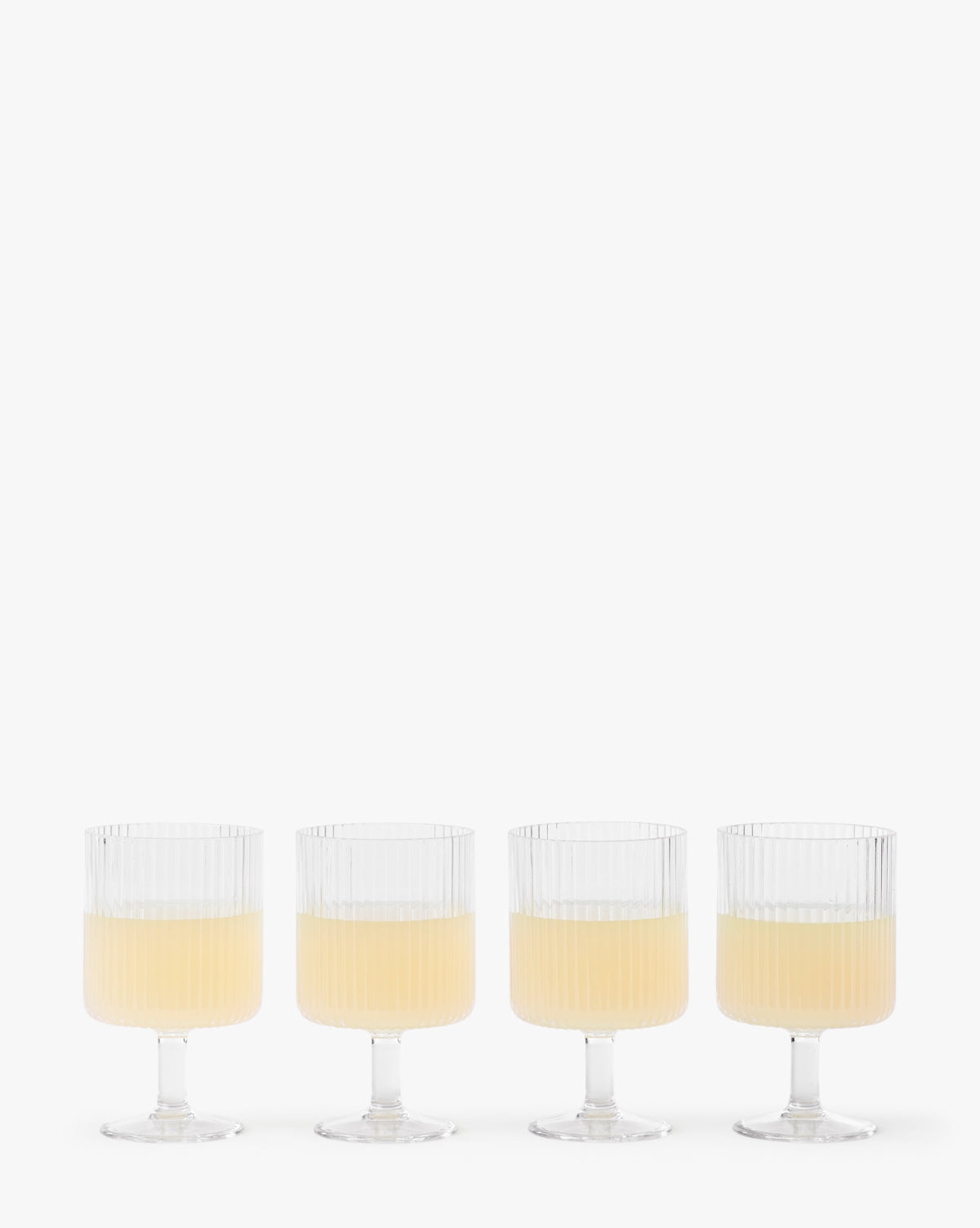 The Sanibel Acrylic Goblets (Set of 4) feature clear, ribbed designs and short stems, each filled halfway with a light yellow drink—ideal for stylish outdoor table settings against a simple white background.