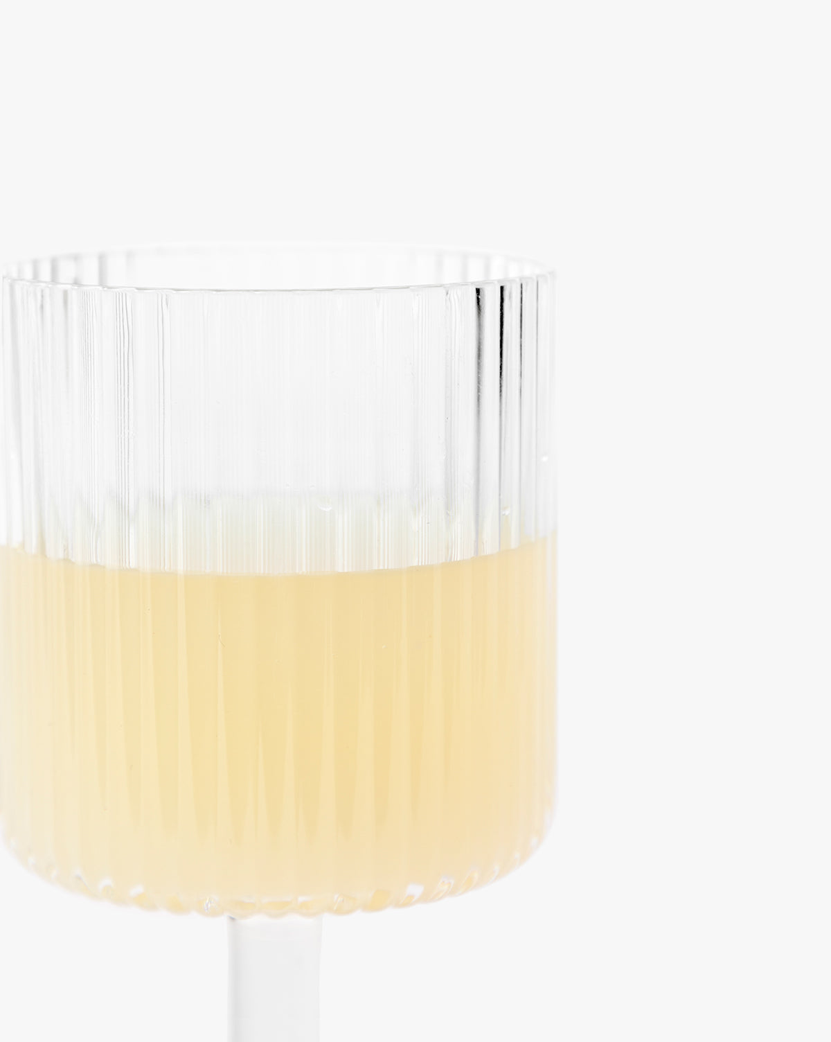 A Sanibel Acrylic Goblet from the set of 4, featuring a ribbed design and filled halfway with a light yellow beverage, is displayed against a plain white background.
