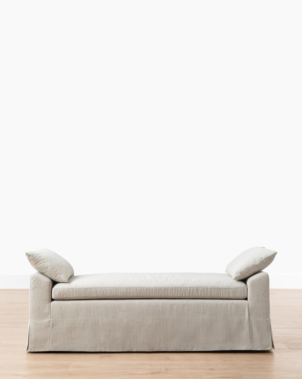 The Makerspalm Scaletta Bench (Ready to Ship) features light gray linen upholstery and includes two matching angled pillows, shown on a wooden floor with a plain white background. Vendixs
