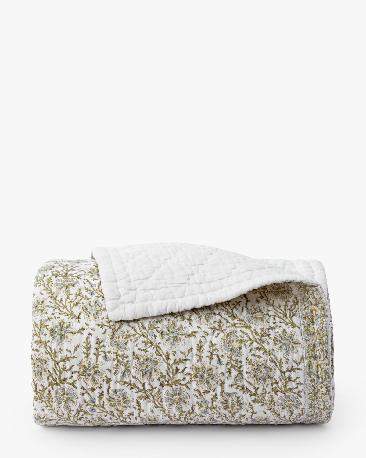The Seton Kids Quilt by Renuka Inc. features a folded white design with green and beige floral patterns and textured stitching. One corner is turned over, revealing the plain white underside. Vendixs