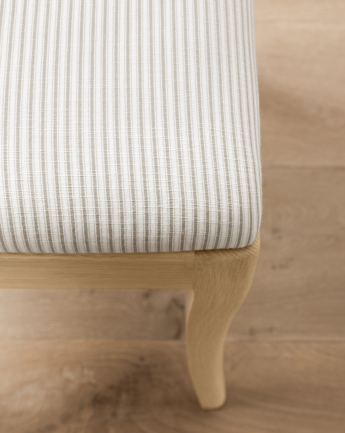 Close-up of the Makerspalm Shepherd Counter Stool, featuring light wood legs and a white seat with thin gray vertical stripes in performance upholstery, set on a light wood floor. Vendixs