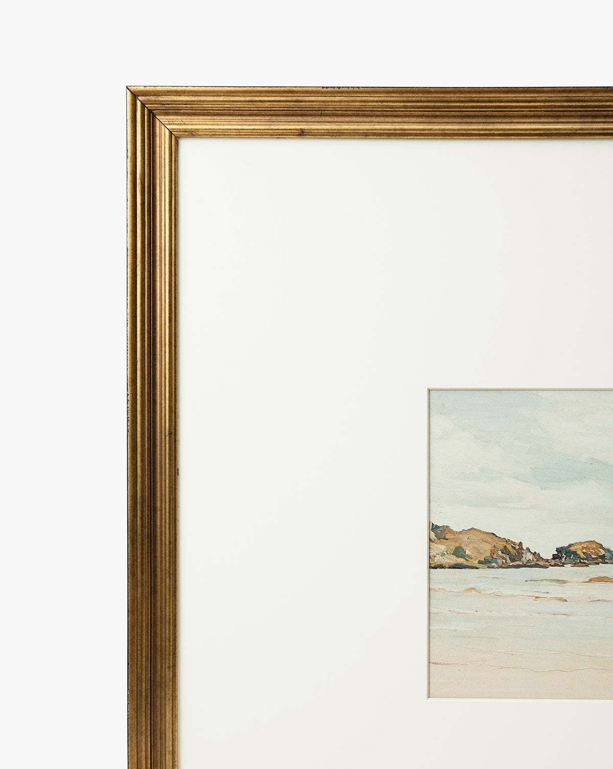 A close-up of the gold-framed Shoreline Rocks giclee print shows a coastal scene with shoreline rocks, sandy beach, and blue sky, set in a white mat. Only the left side of the frame and artwork are visible, by Vendixs