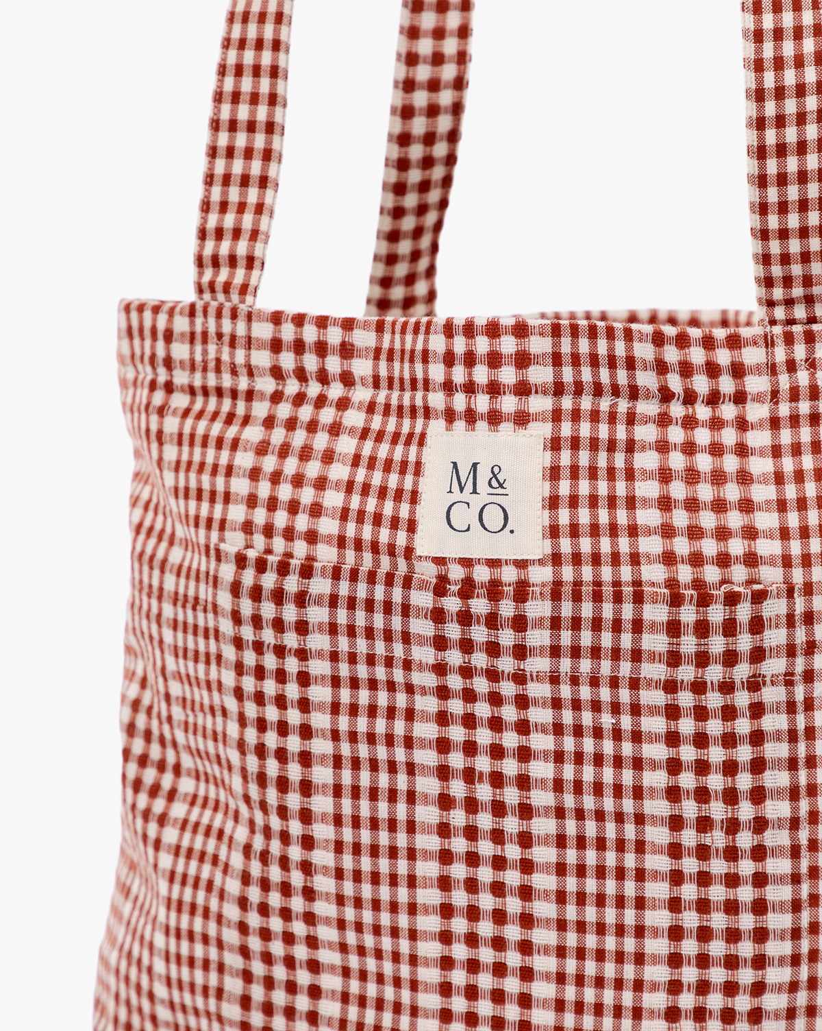 Close-up of the Spencer Tote Bag, featuring red and white gingham fabric and two handles. A small white label near the top displays "M & CO." in black letters, by Vendixs
