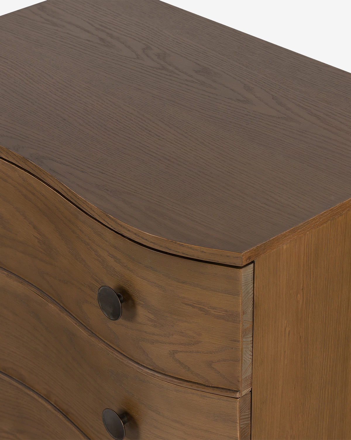 A close-up of the Strasburg Nightstand shows its natural wood finish, curved drawer fronts, and round dark metal knobs—an antique-inspired piece ideal for timeless bedroom style, by McGee & Co.
