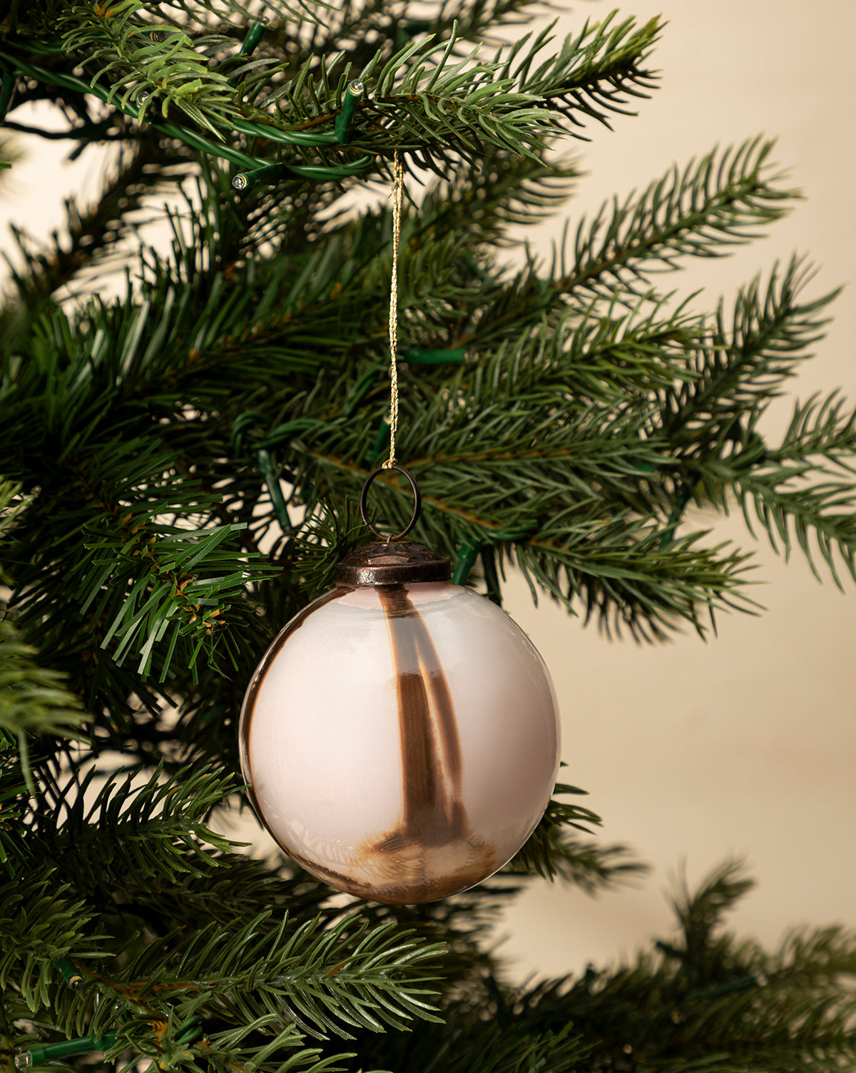 The 4" Striped Glass Bauble, a round metallic ornament with gold stripes, hangs from a string on a green holiday tree surrounded by pine needles, set against a neutral background, by Vendixs