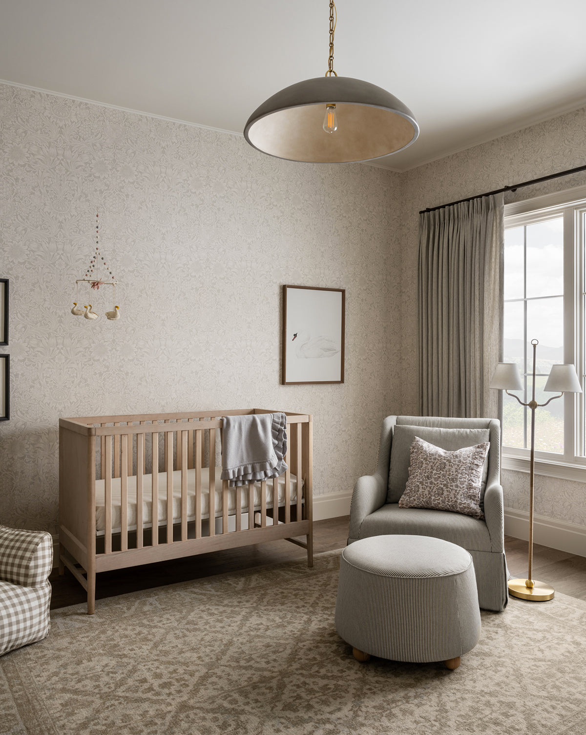 A cozy nursery featuring a light wood crib, gray armchair with ottoman, neutral patterned rug, soft curtains, swan wall art, animal mobile, jute rope accents, the Sirocco Floor Lamp, and plenty of natural light from a large window, by Vendixs