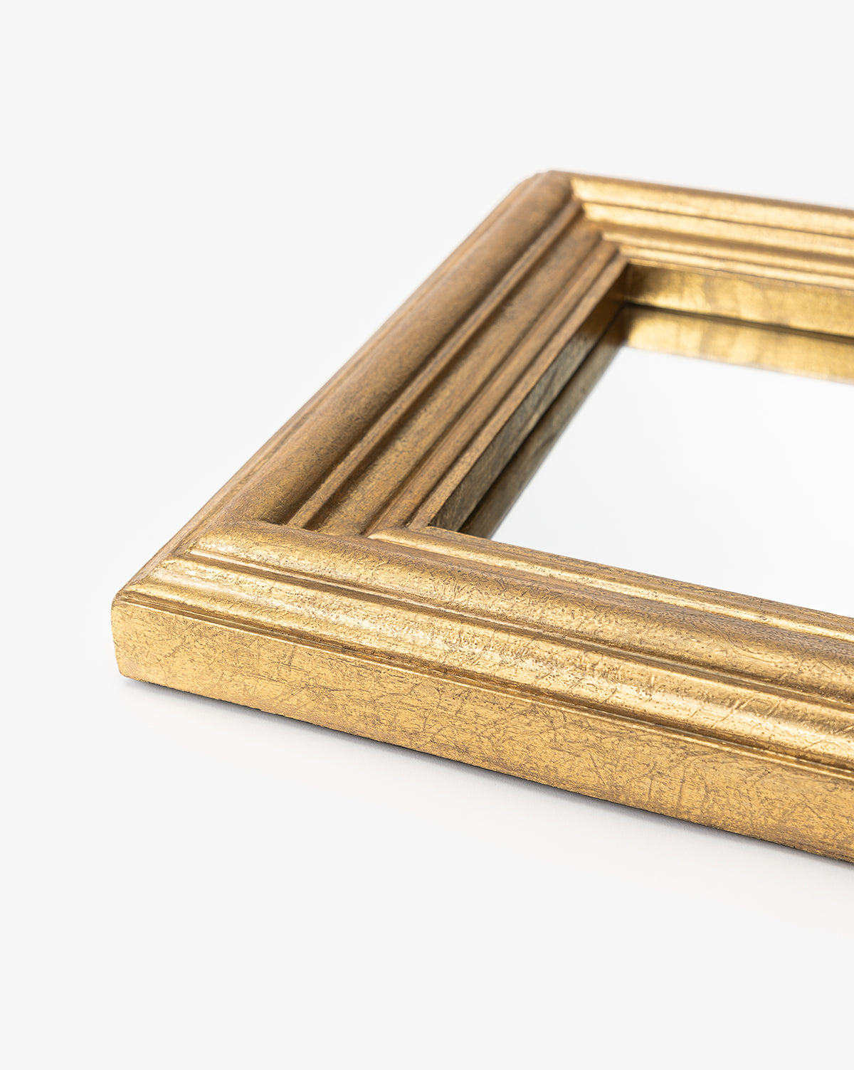 A close-up of the Suzanne Shelf Mirrors gold-finished frame with ridged detailing, shown against a plain white background, by Vendixs