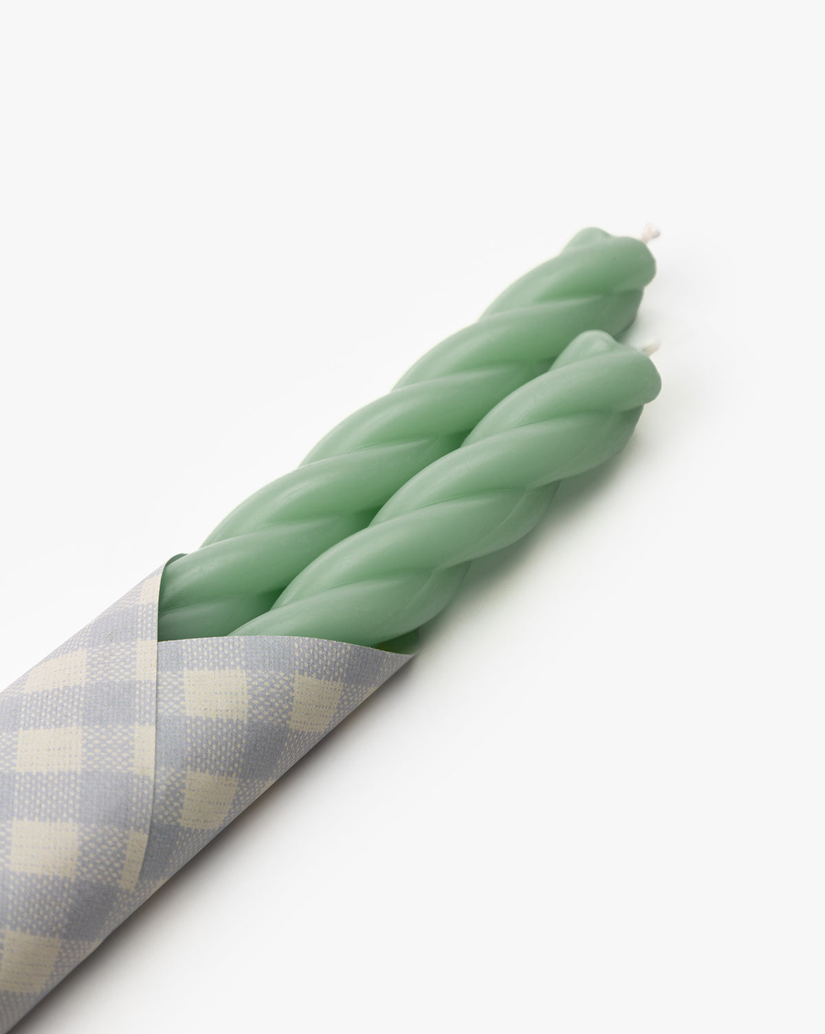 The Vendixs x Loeffler Randall Sybil Wax Taper Candles (Set of 2) in pastel green are partially wrapped in gray and white checkered paper, displayed on a plain white background by Vendixs