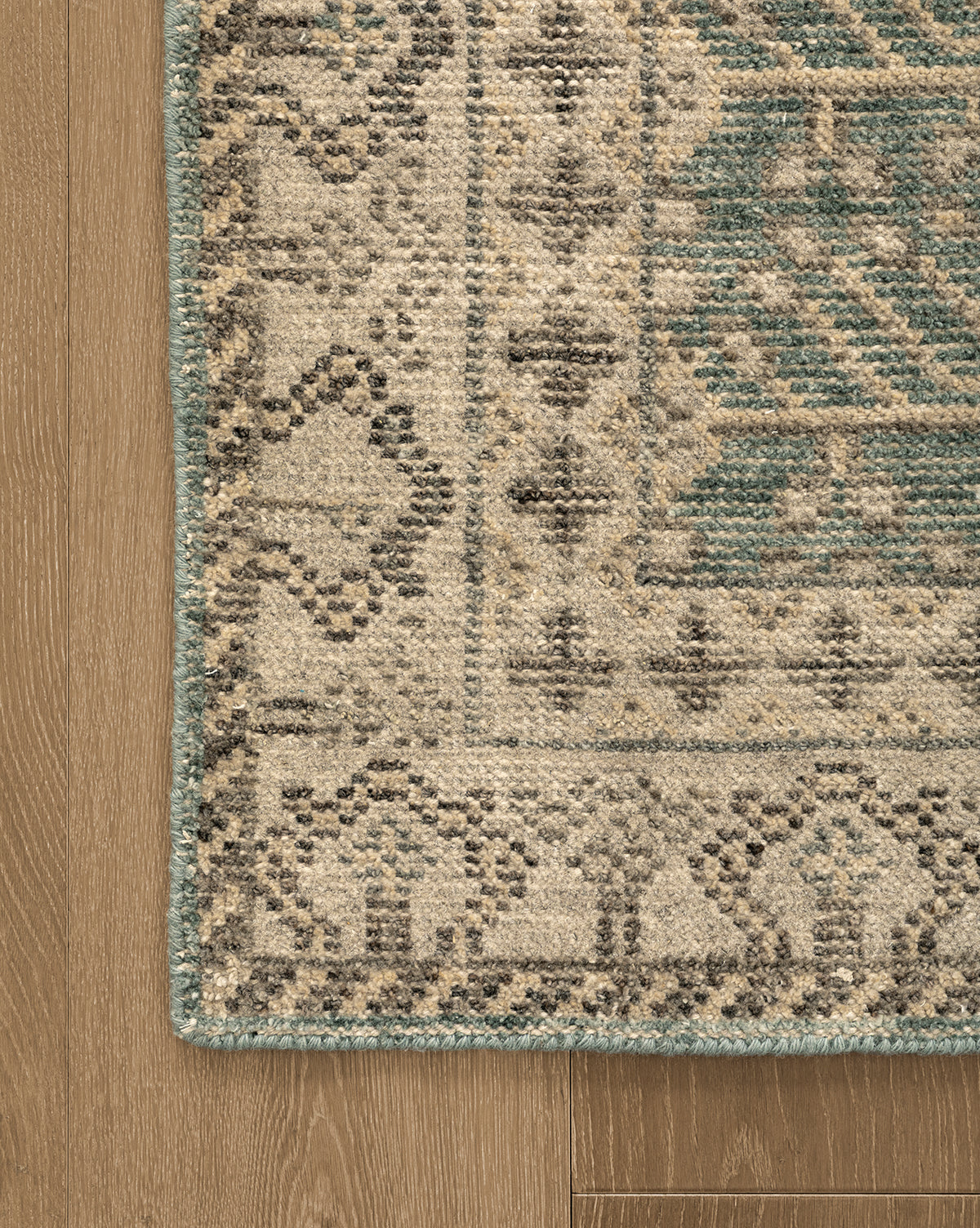 Corner of the Thames Hand-Knotted Rug with beige, green, and dark gray geometric designs on light brown wood flooring—a timeless addition to luxury home decor, by McGee & Co.
