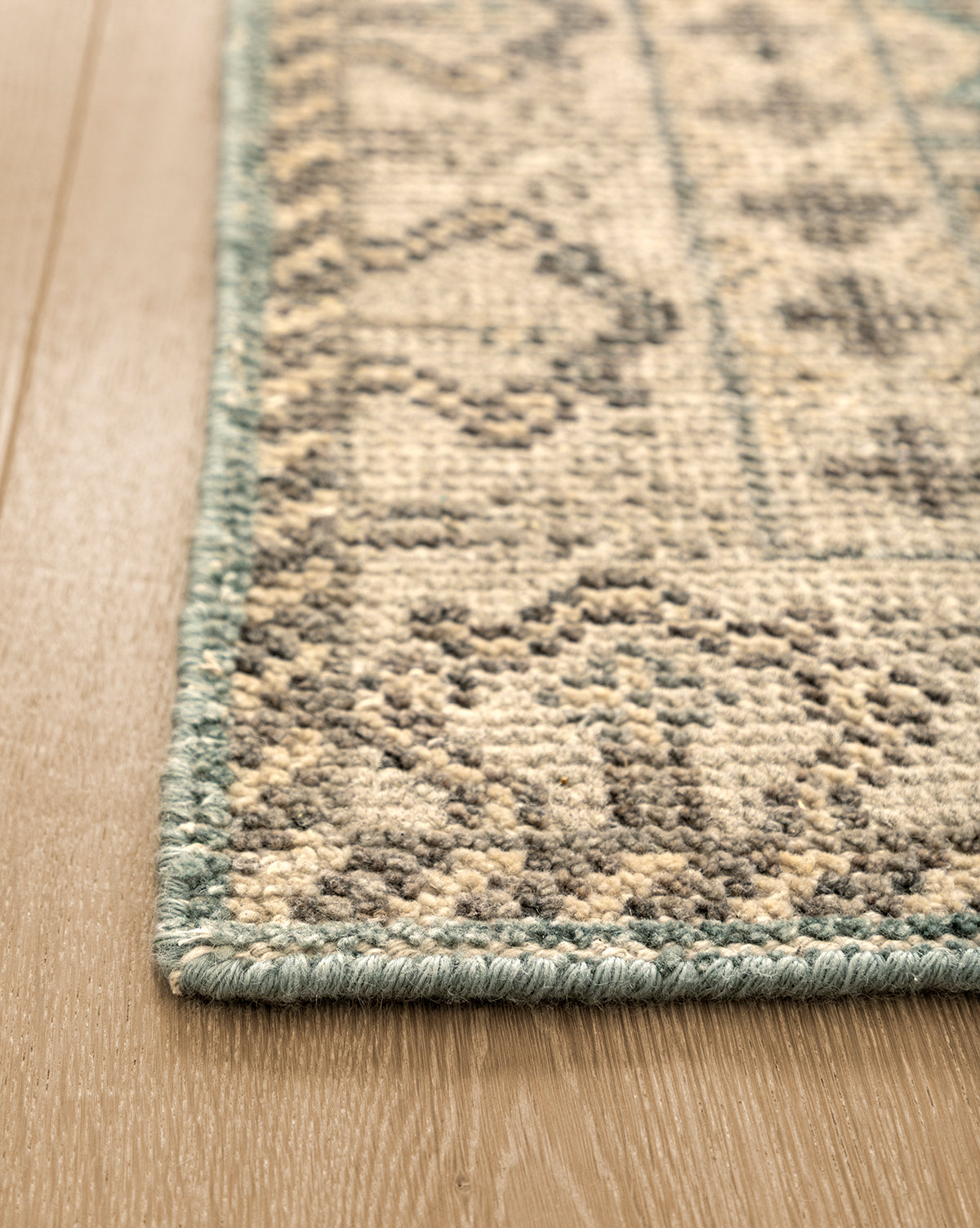 Close-up of the Thames Hand-Knotted Rug, featuring a thick pile and teal border on a light wooden floor. Beige and gray geometric patterns add elegance—ideal for luxury home decor, by Vendixs