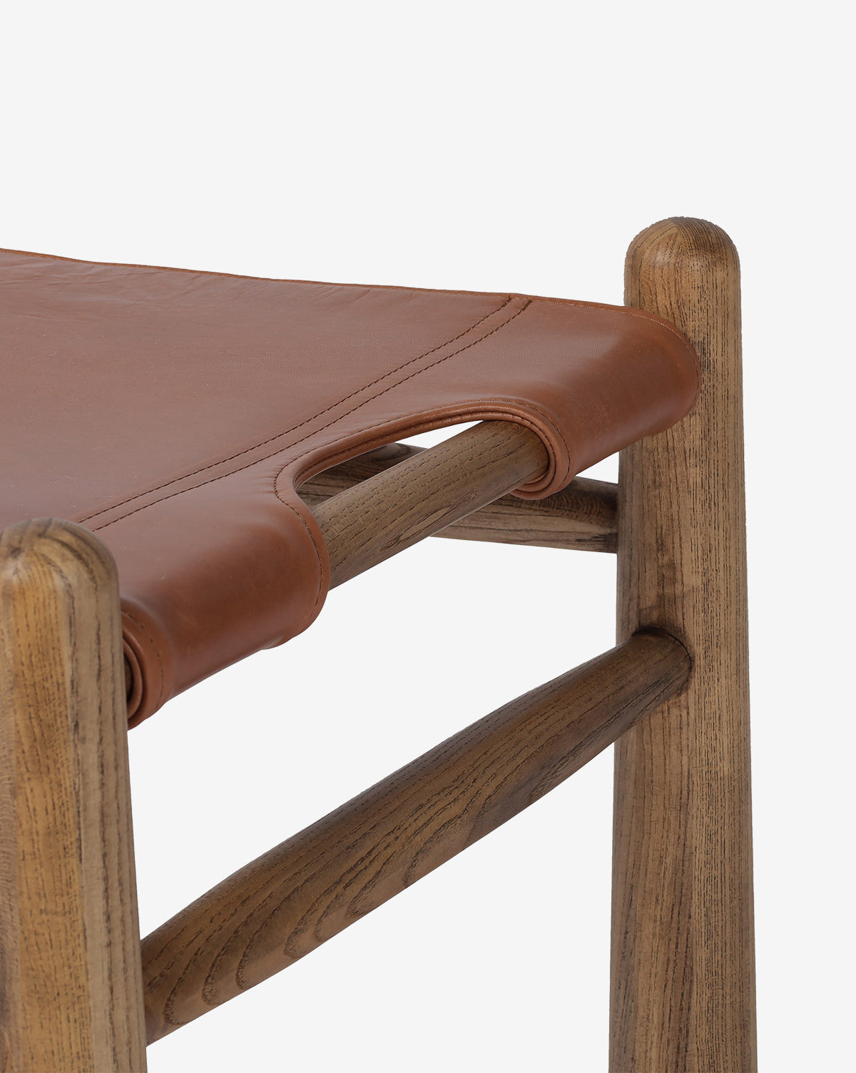 Close-up of the Tierney Ottoman by Four Hands: features a smooth, natural-finish solid wood corner and a brown top grain leather seat with stitched handle detail. Vendixs
