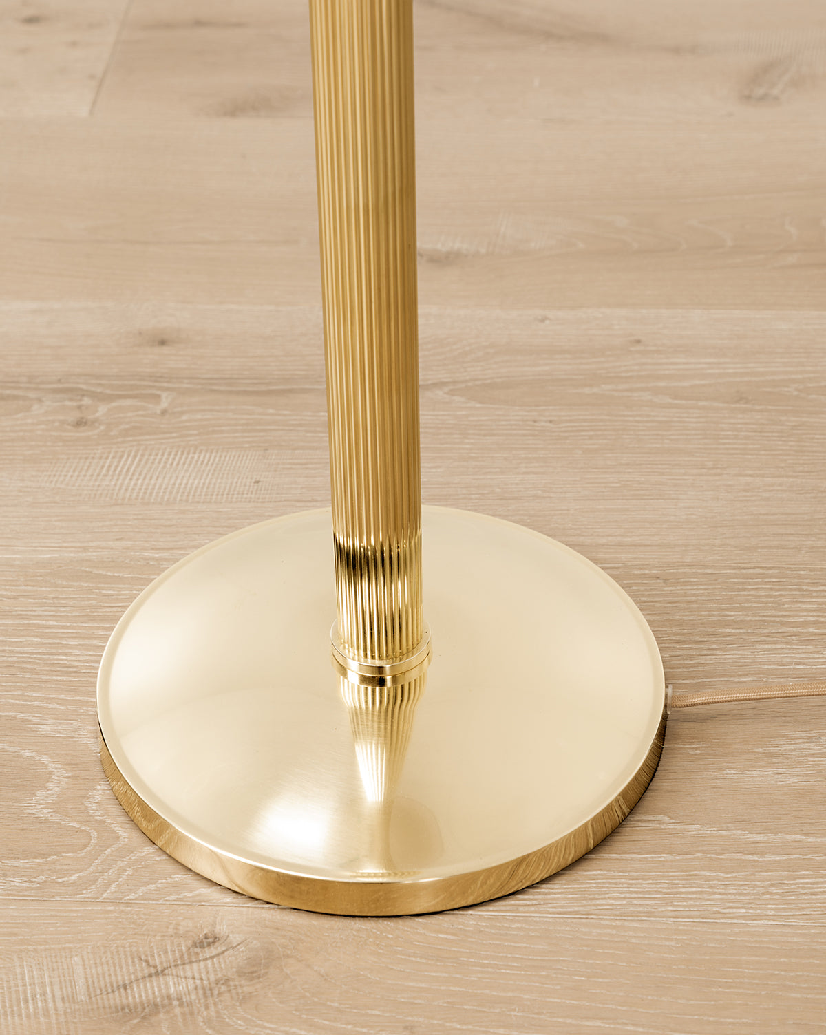 A close-up of the Townes Floor Lamp’s shiny, reeded brass base with a ribbed pole, standing on a light wood floor, by Vendixs
