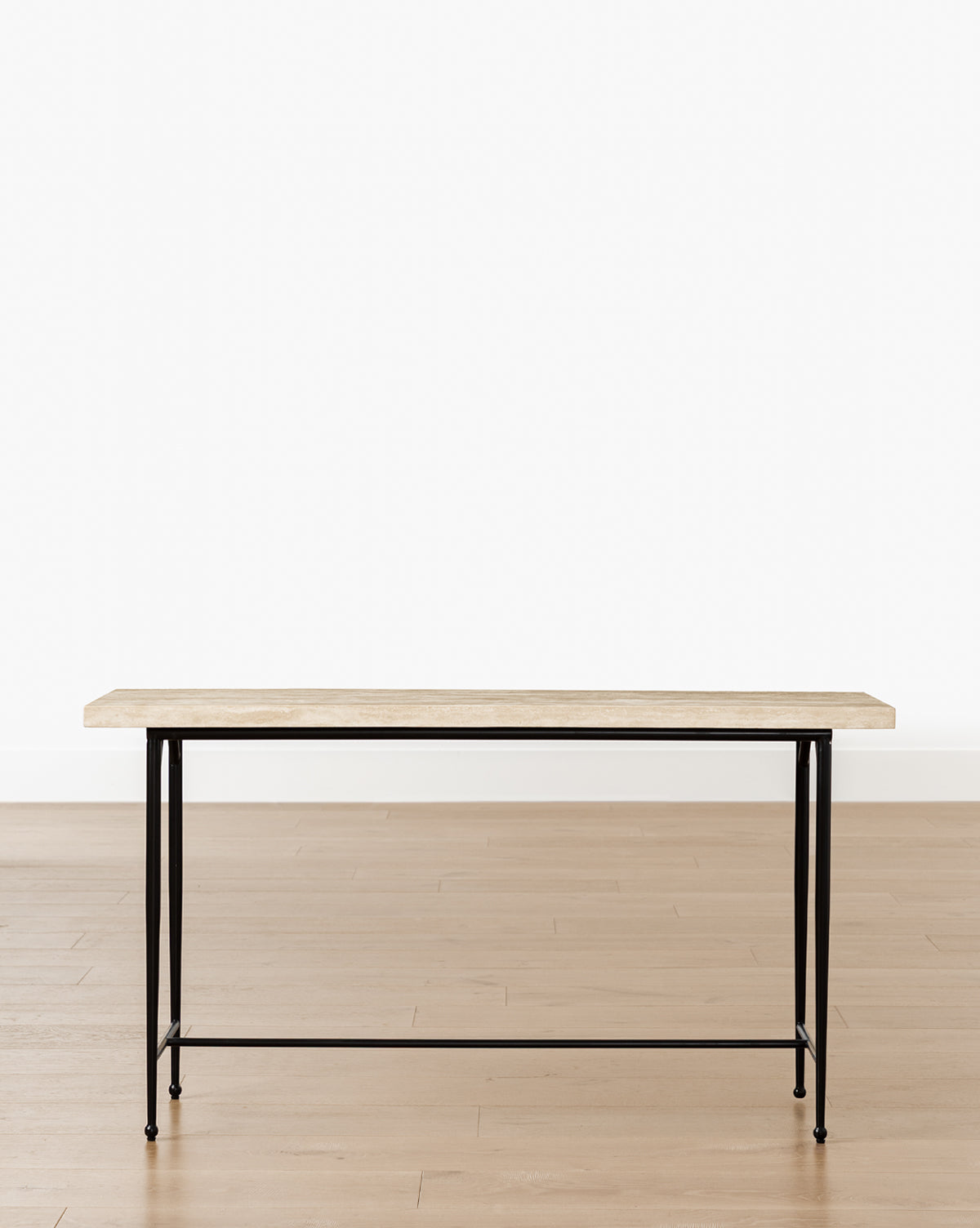The Travertine Console features a minimalist design with a light wood top and slender black hand-forged iron legs, displayed on a light wood floor against a plain white background by Vendixs