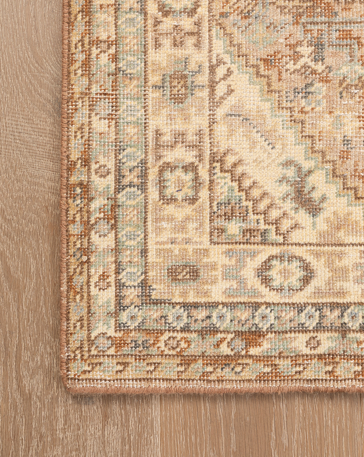 A close-up of the Tulie Hand-Knotted Wool Rug shows its traditional beige, tan, blue, and brown geometric pattern with a detailed border, resting on a light wood floor, by Vendixs