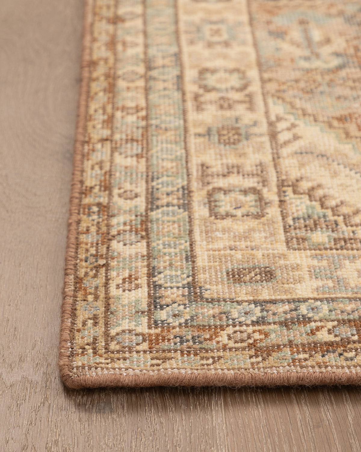 Close-up of the Tulie Hand-Knotted Wool Rug, showcasing its beige, brown, and blue geometric pattern with a detailed traditional border. The rug is displayed on a light wood floor, by Vendixs