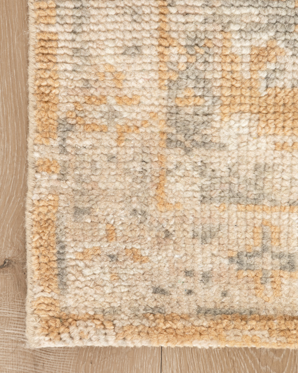 A close-up of the Vanderwood Hand-Knotted Wool Rug shows its thick pile and subtle geometric designs in beige and tan earth tones, lying on a light wooden floor, by Vendixs