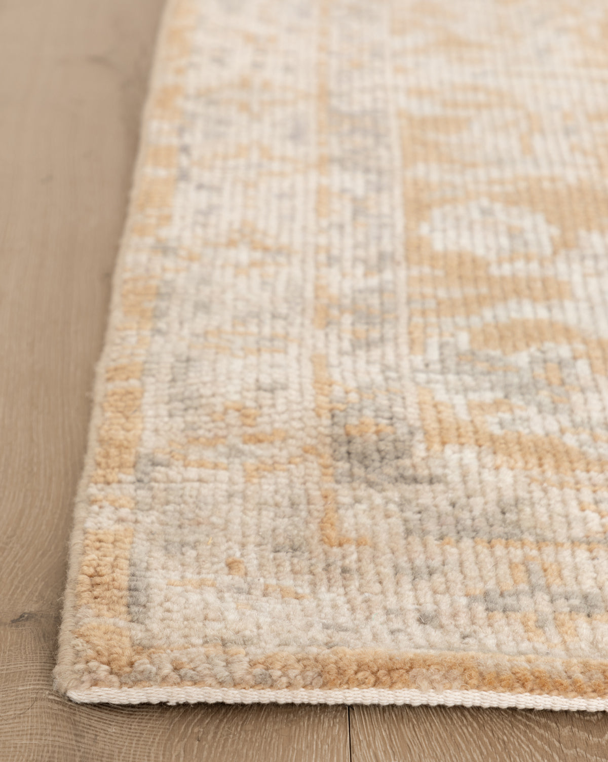 Close-up of the Vanderwood Hand-Knotted Wool Rug in beige and light brown on a light wooden floor, highlighting its soft wool texture and subtle geometric design, by Vendixs