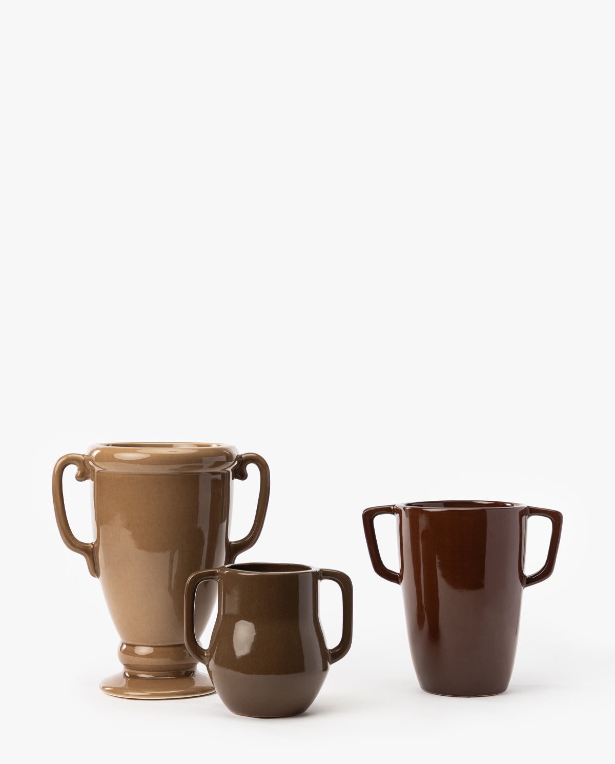 Three Victoire Vases in brown ceramic, each varying in shape and size, are arranged side by side on a white background, with the tallest vase on the left and the smallest earthenware piece in the center, by Vendixs