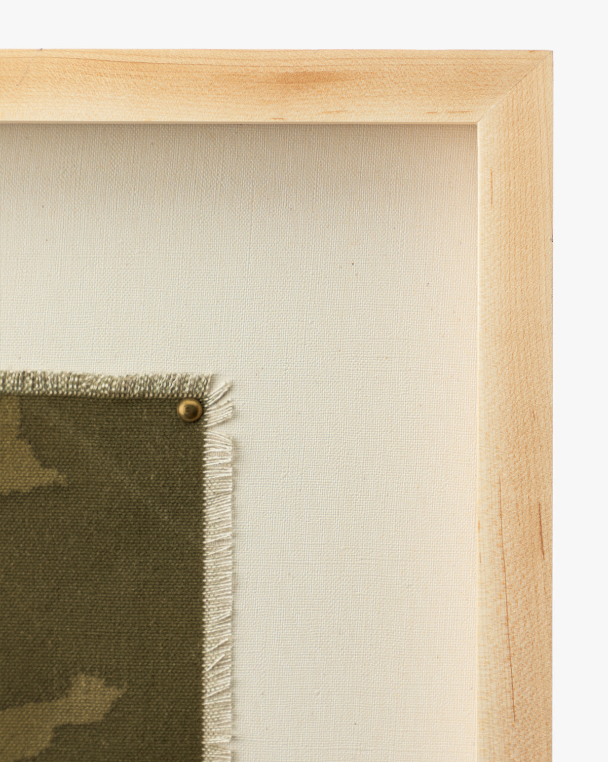 Close-up of the light oak frame for Viewpoint by Britney Schulz, showcasing museum-quality canvas with green patterned fabric, frayed edges, and a brass tack, all set against a plain off-white background by Vendixs