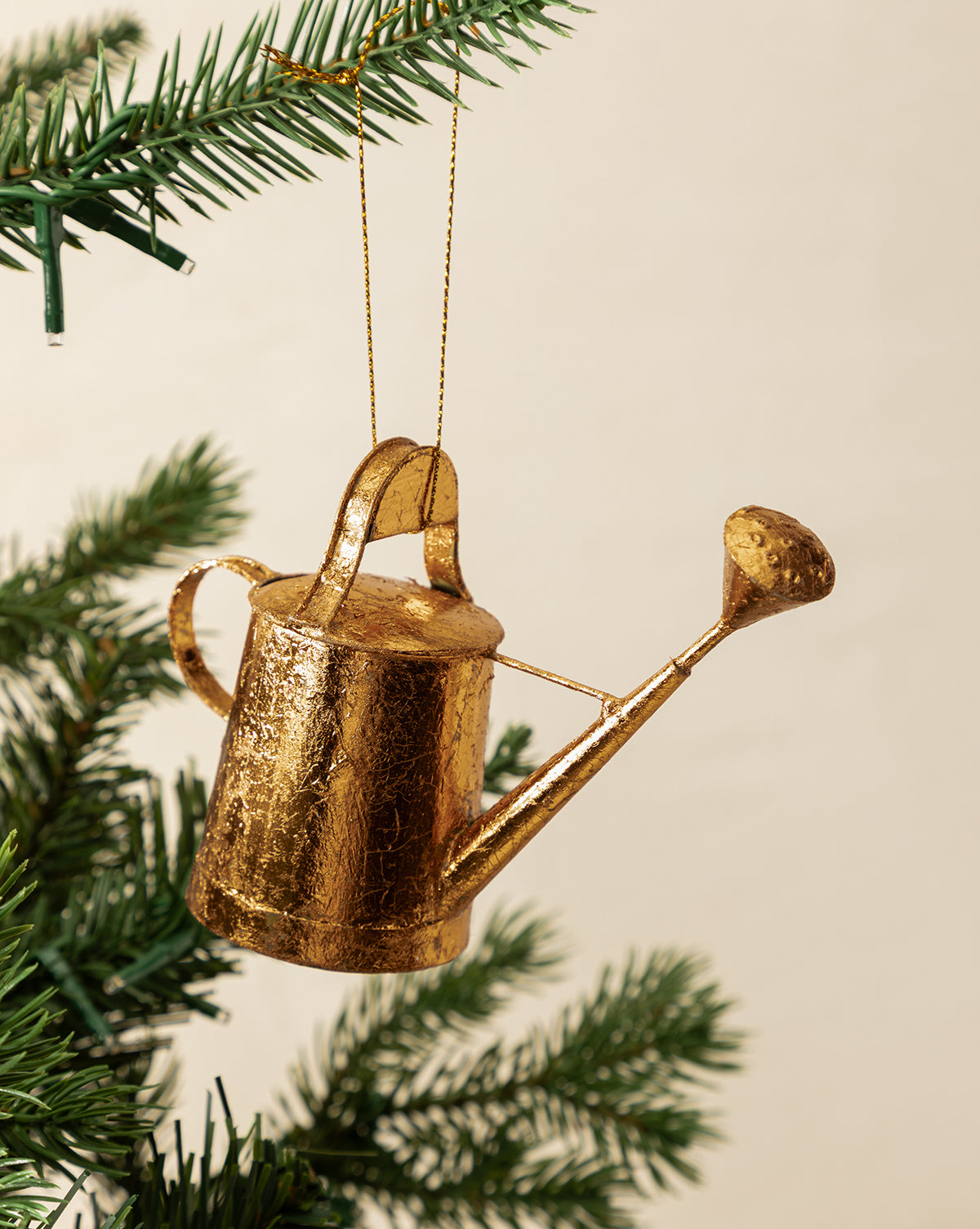 The Watering Can Ornament with a copper finish hangs from a string on a green Christmas tree branch, bringing festive charm to the holiday decor, by Vendixs