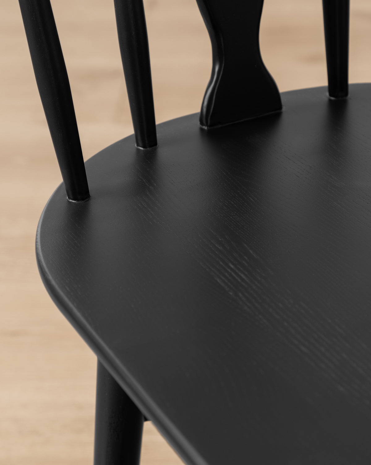 Certainly! Here’s your blended sentence: Close-up of the Whittaker Counter Stool by YANG CHENG WOODEN INDUSTRIES INTERNATIONAL (VIETNAM) CO LTD, showcasing its smooth black solid oak seat and vertical spindle back against a light wood floor. Vendixs