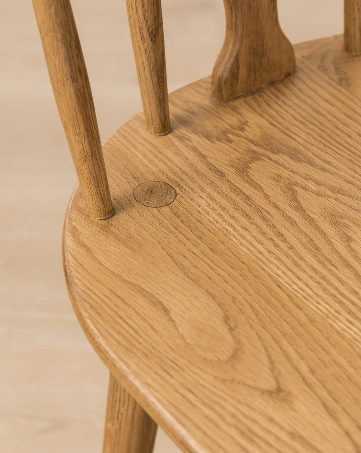 Close-up of a Whittaker Counter Stool by YANG CHENG WOODEN INDUSTRIES INTERNATIONAL (VIETNAM) CO LTD, featuring a smooth solid oak seat with light brown finish, visible wood grain, round peg detail, and classic spindle backrest. Vendixs