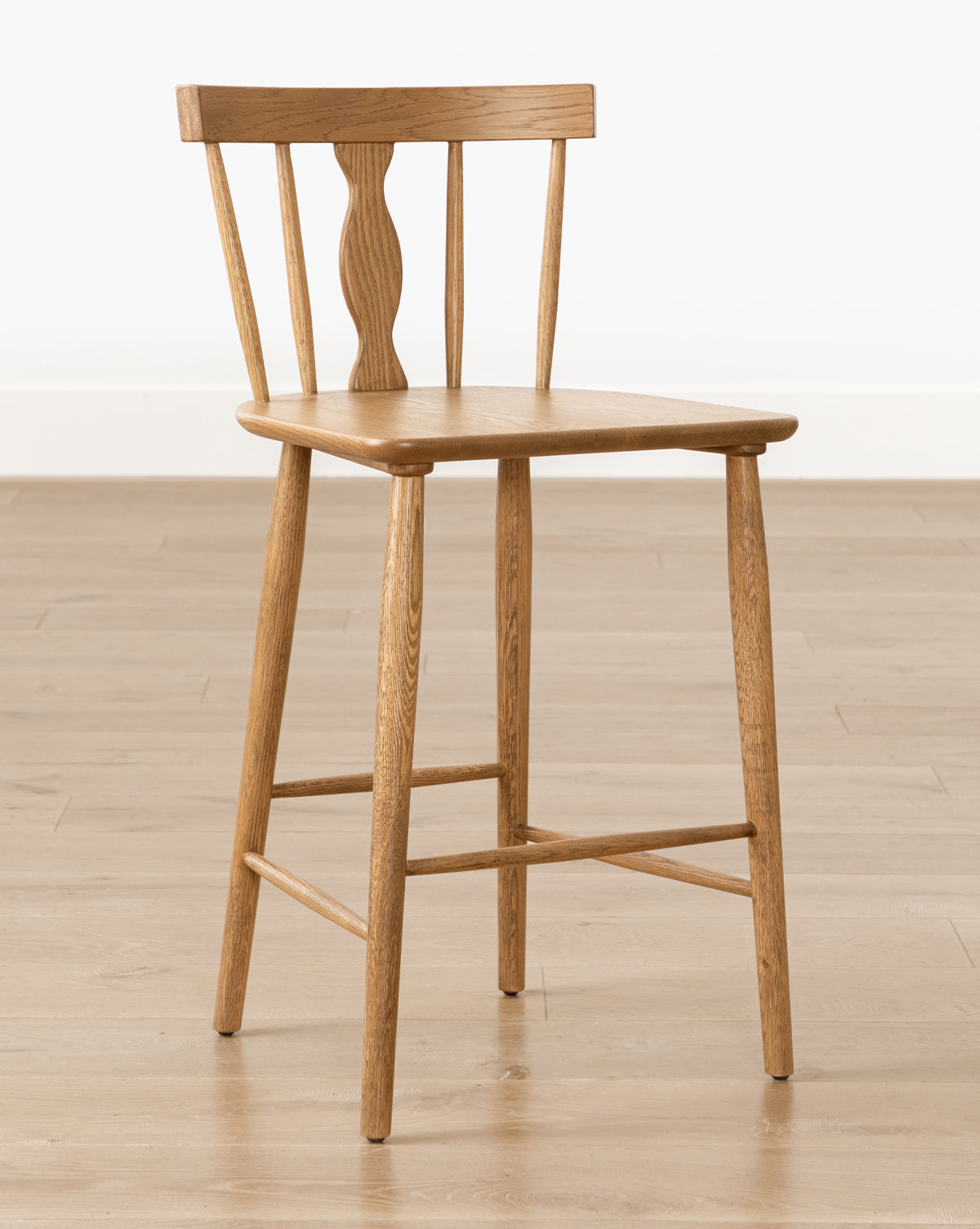 The Whittaker Counter Stool by YANG CHENG WOODEN INDUSTRIES INTERNATIONAL (VIETNAM) CO LTD features a spindle back design and four straight legs, shown on a light wood floor against a plain white wall. Vendixs