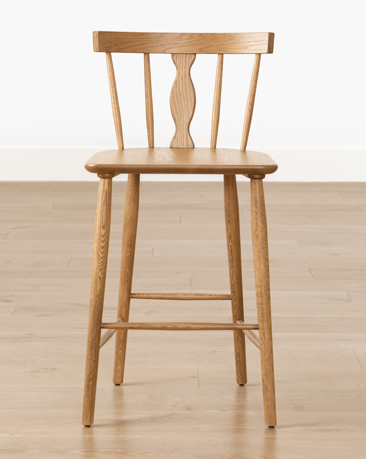 A Whittaker Counter Stool by YANG CHENG WOODEN INDUSTRIES INTERNATIONAL (VIETNAM) CO LTD, with a solid oak finish and spindle back design, stands on a light wood floor against a plain white background. Vendixs
