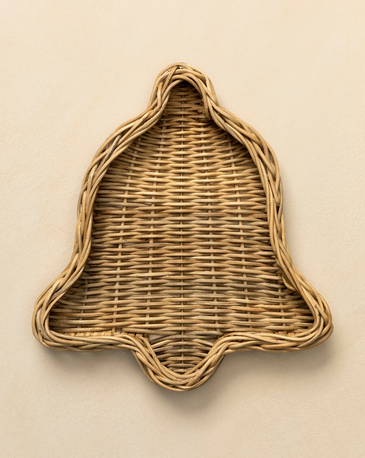 The Wicker Bell Tray, handwoven in a festive bell shape and ideal for holiday entertaining, is displayed on a light beige surface, by Vendixs