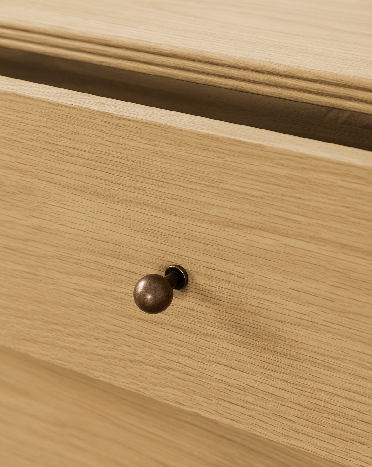 Close-up of a partially open Wilkins Oak Nightstand drawer, featuring a round bronze knob and light wood finish—ideal for enhancing your bedroom décor, by Vendixs