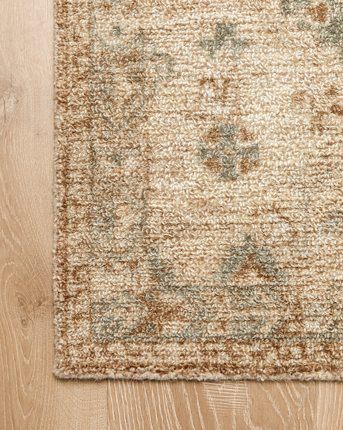 A close-up of the Wilshire Natural Hand-Tufted Wool Rug on a light wood floor highlights its subtle floral design, textured fibers, and spill-resistant surface for easy maintenance, by Vendixs
