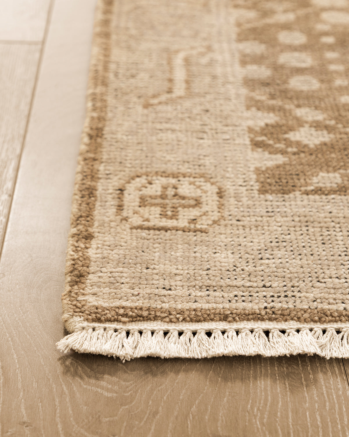 Close-up of the Windsor Hand-Knotted Wool Rug in beige, featuring geometric patterns and fringe along one edge on light wood flooring. The wool texture and intricate weave details are clearly visible, by McGee & Co.