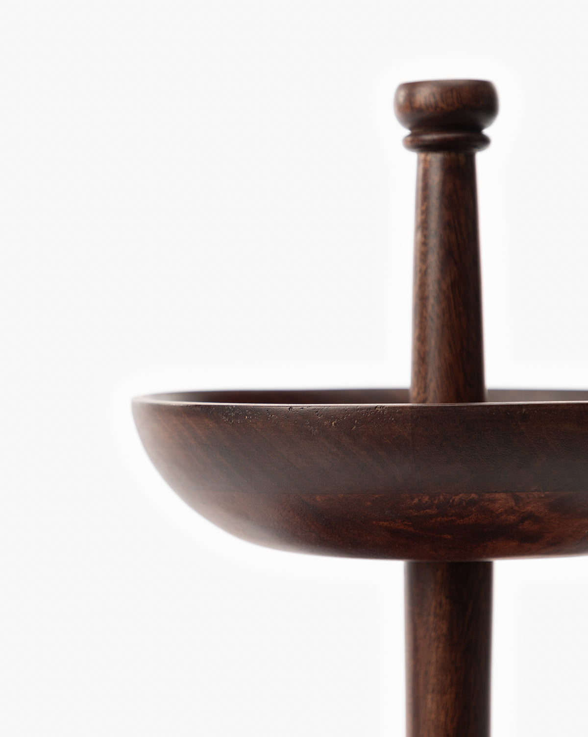 Close-up of the Winward Tiered Pedestal, a dark wood tray with a raised central handle, displayed against a plain white background. Only part of its sculpted design is visible, emphasizing minimalism, by Vendixs