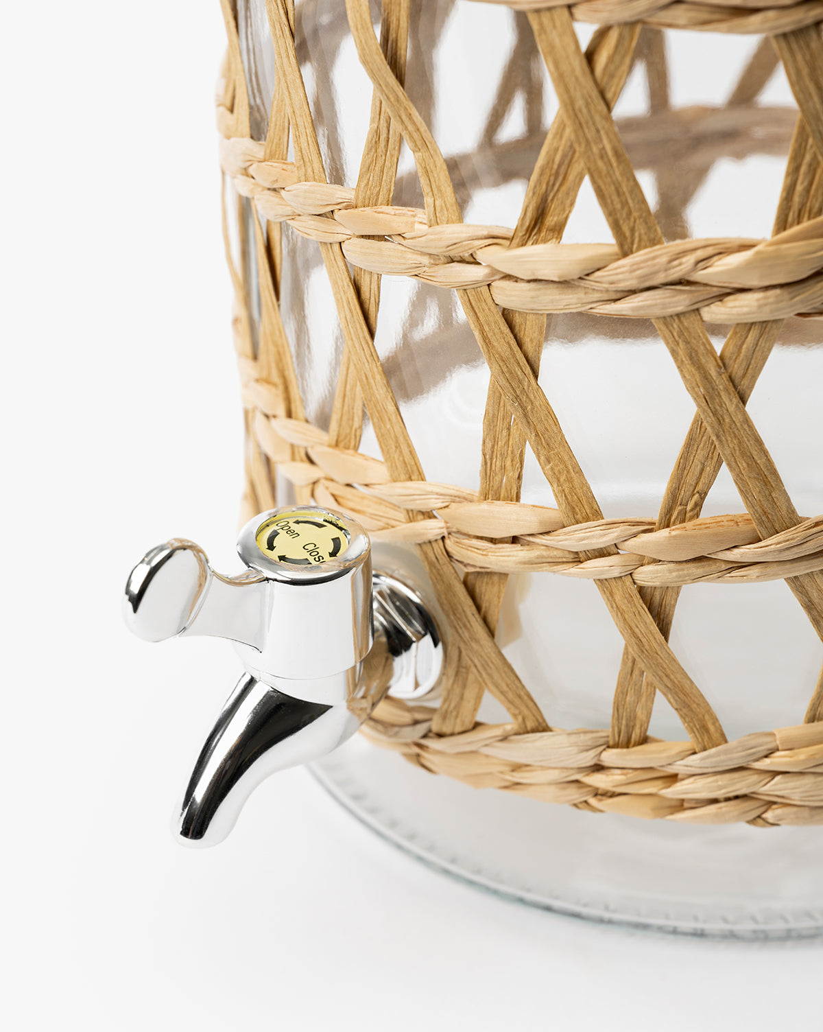 Close-up of the Glass Beverage Dispenser with Woven Sleeve, featuring a shiny silver spigot and a seagrass-wrapped design, set against a plain white background, by Vendixs