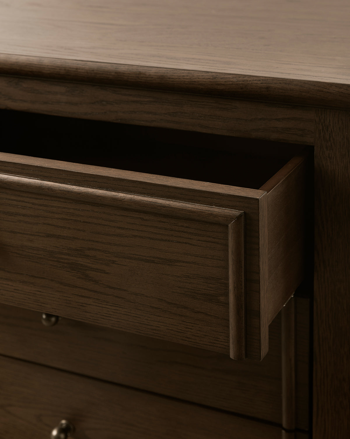 A close-up of the Yorkshire Nightstand with one drawer partially open, showcasing the smooth, dark wood grain and antique brass pulls on the lower drawers, by Vendixs
