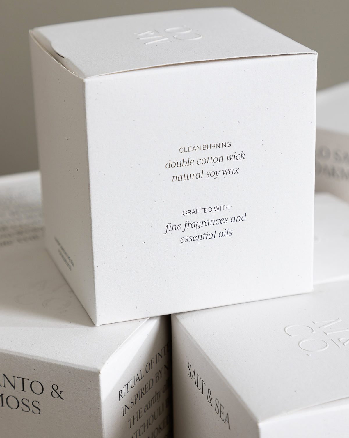 A white candle box with minimalist text describes the Palo Santo & Oakmoss Candle—clean burning, double cotton wick, crafted with fine fragrances and essential oils. Similar boxes, like an essential oil candle, are partially visible underneath by Vendixs