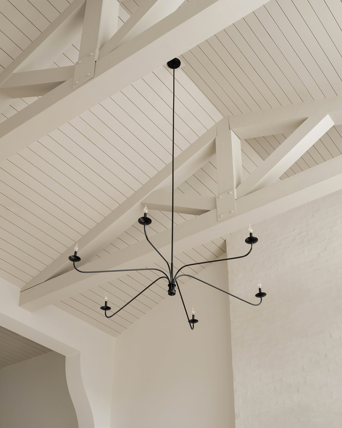 The Makerspalm Philomena Chandelier features six candle-style lights and blends classic and modern design, making it a striking addition to bright, airy rooms with high, white, vaulted ceilings and exposed beams by Vendixs