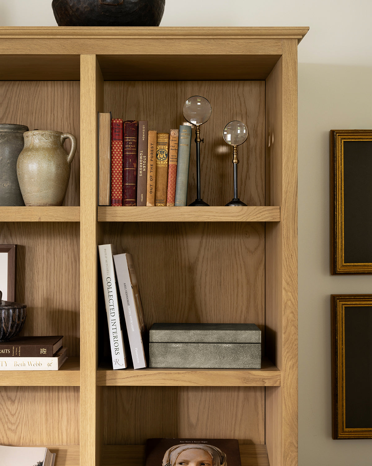 A wooden bookshelf showcases ceramic vases, a row of books, the Barnabas Standing Object, a decorative box, and partly visible framed pictures—perfect for curated home decor, by Vendixs