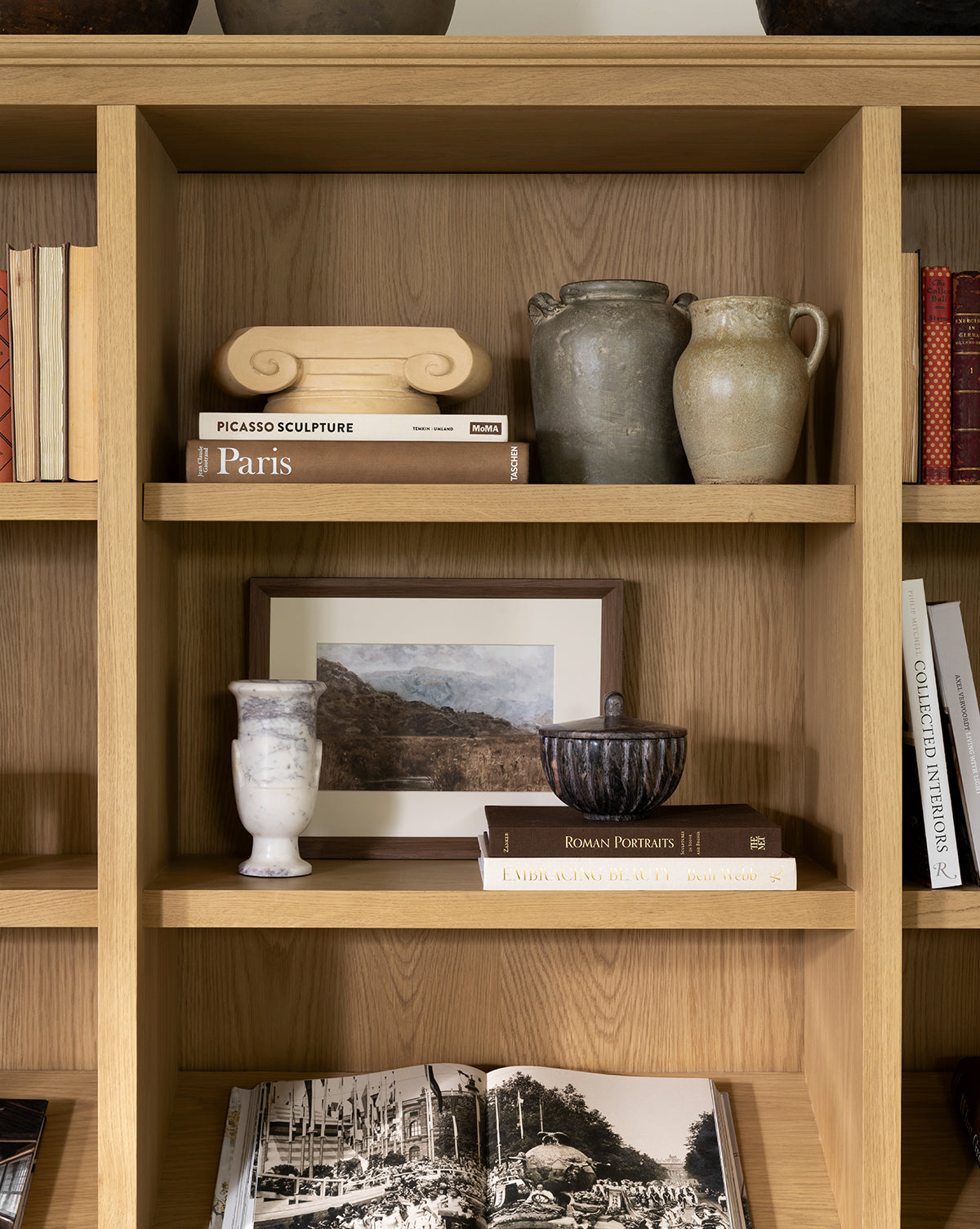 Wooden bookshelf with ceramic vases, decor pieces, and art books like Paris and Picasso Sculpture, featuring Marshland giclee on paper in a walnut woodgrain frame displayed on the middle shelf, by Vendixs