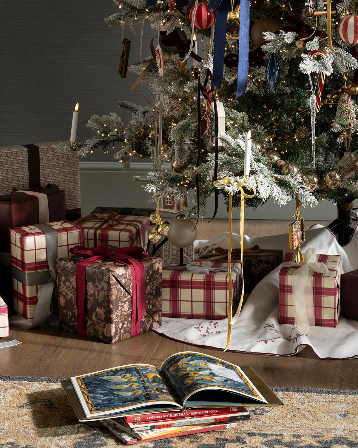 A Christmas tree with plaid and gold ornaments stands over presents wrapped in Highland Plaid Gift Wrap, while a festive book lies open on a white tree skirt in front of the gifts, by Vendixs
