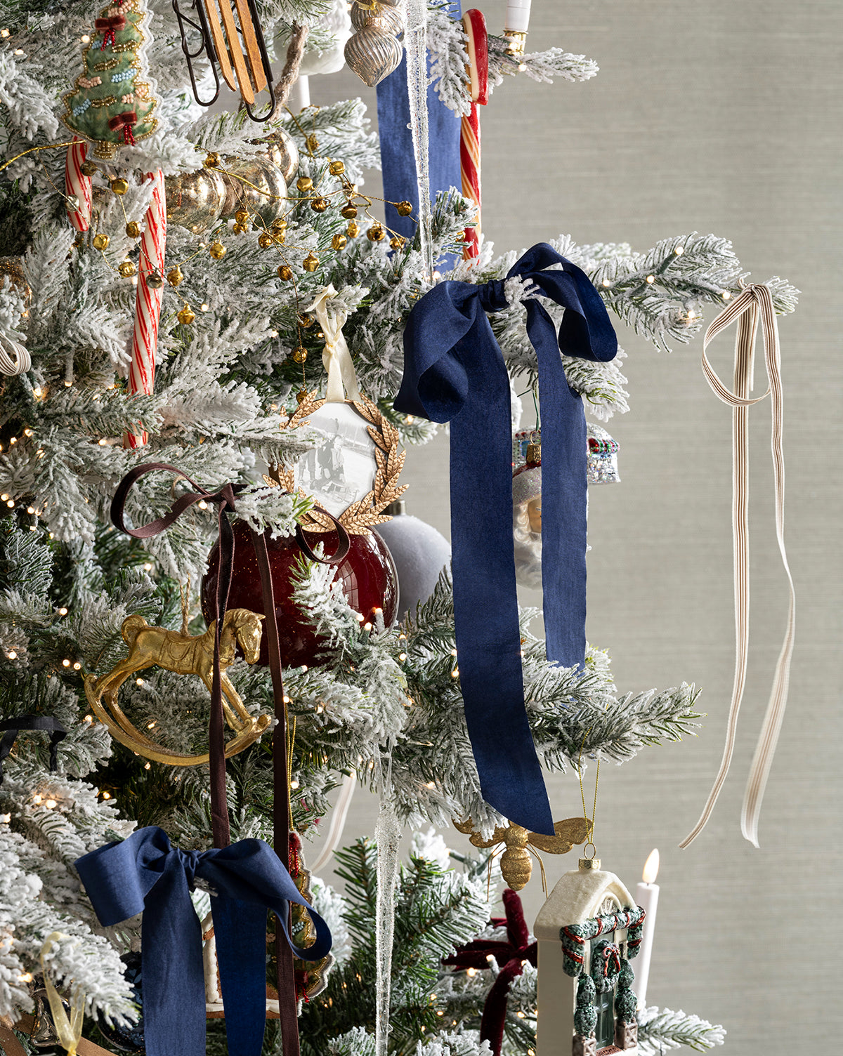 A snow-dusted Christmas tree decorated with blue and brown ribbons, candy canes, gold and red ornaments, a rocking horse ornament, hanging candles, and the Laurel Picture Frame Ornament, by Vendixs