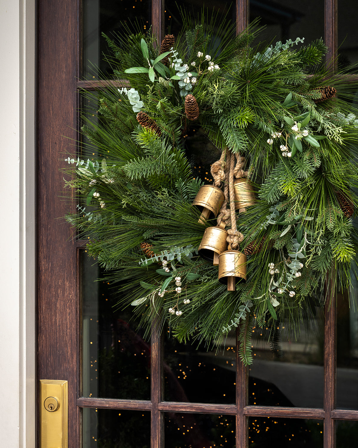 The 24" Pinecone & Berries Faux Wreath features pine needles, pinecones, white berries, and three gold bells tied with rope at the center—perfect festive decor for your door, by Vendixs