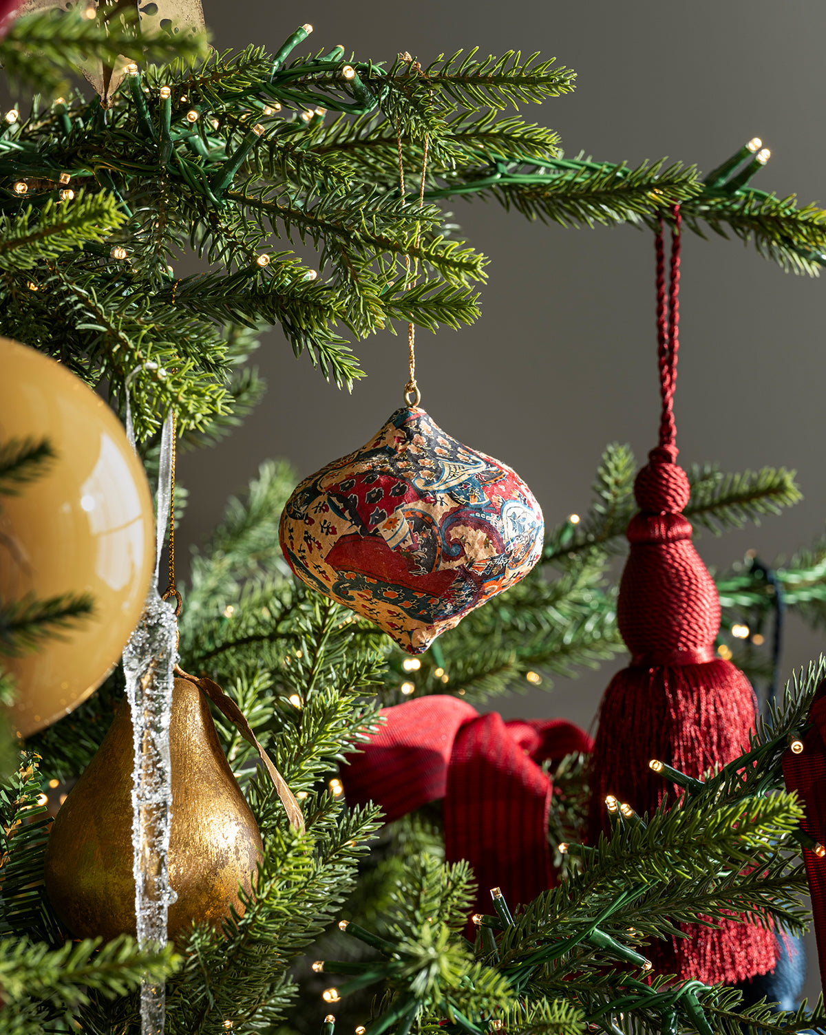 Close-up of the Classic Christmas Tree highlighting a designer mix of colorful patterned ornaments, a gold pear, clear icicle, red tassels, and warm white lights on lush branches, by Vendixs