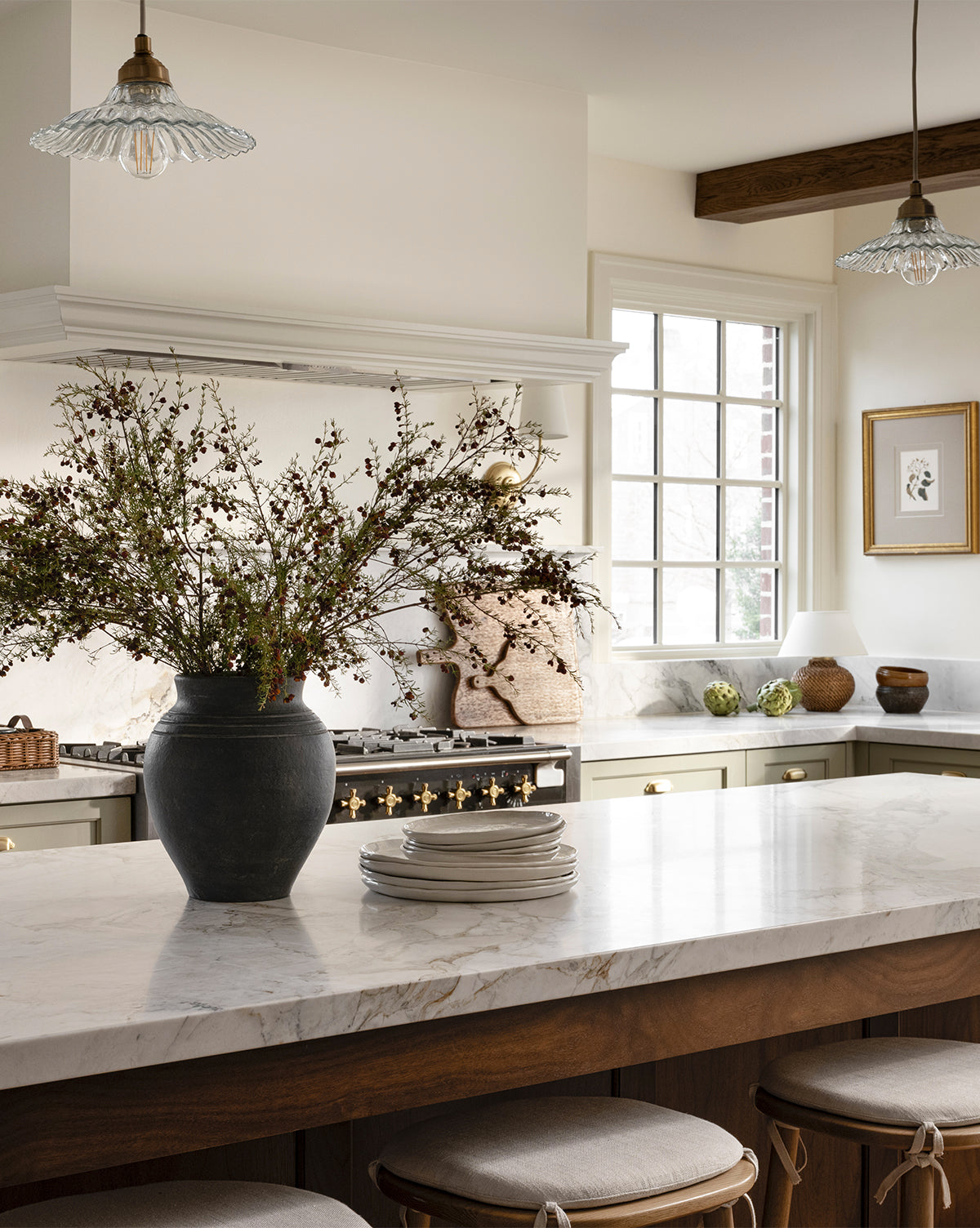 A bright, elegant kitchen with a large marble island, the Ethel Vase filled with branches, stacked plates, stylish light fixtures, and a sunlit window. Warm neutrals and wood accents create a cozy rustic home decor vibe by Vendixs