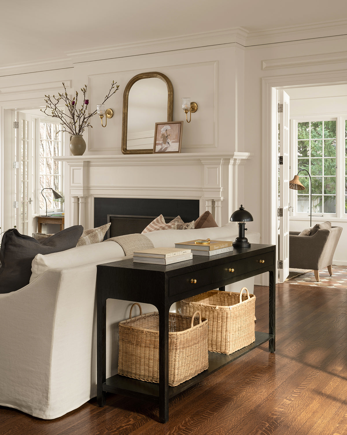 Bright living room with white walls, dark wood floors, a white sofa, black console table with baskets, fireplace topped with a mirror and decor, large windows for natural light, and a Totie Task Lamp beside the sofa by Vendixs