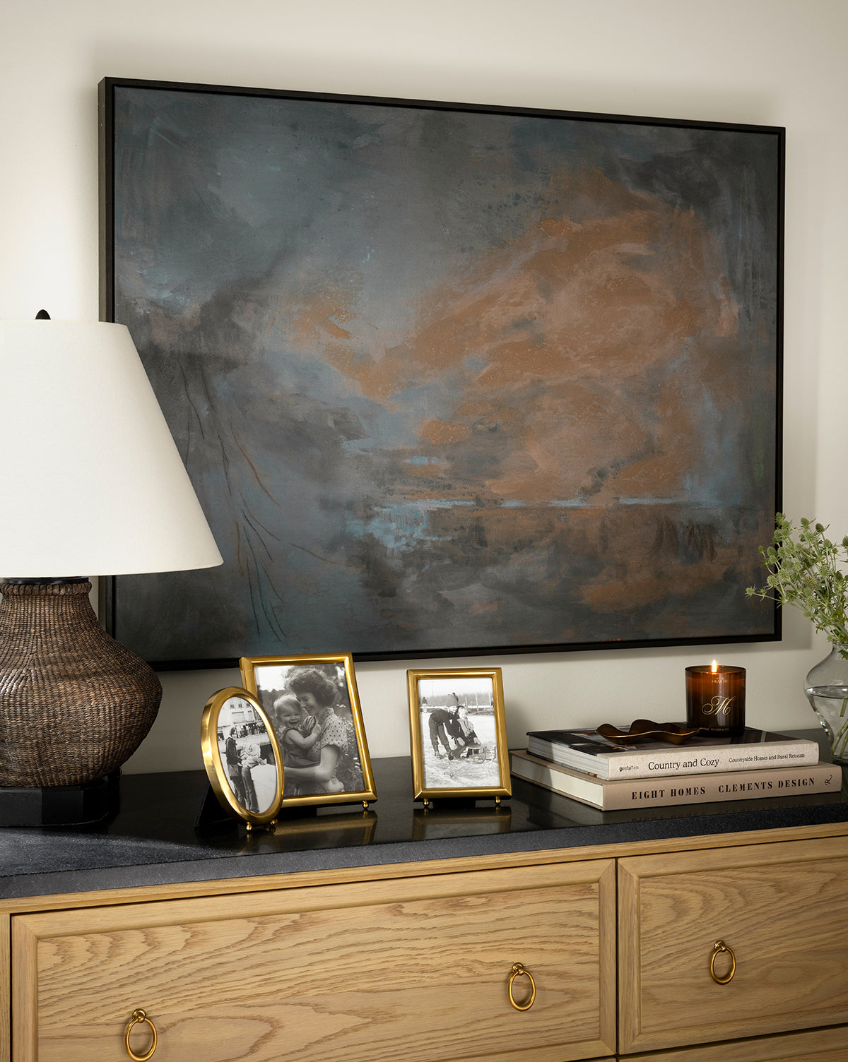 A dresser displays a table lamp, Blanche Picture Frame, stacked books, a candle, and a small flower vase, beneath a large abstract painting on the wall, by Vendixs