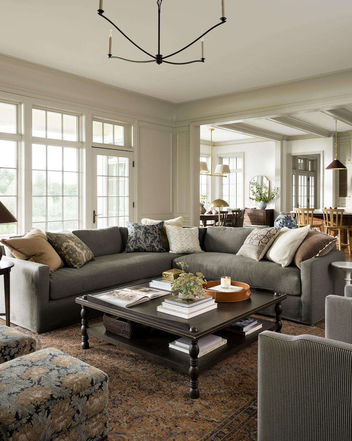 A spacious living room features a large gray sectional, patterned pillows, and dark wood coffee table atop the Piedmont Hand-Knotted Wool Rug. Natural light pours in from large windows, with the dining area visible in the background, by Vendixs