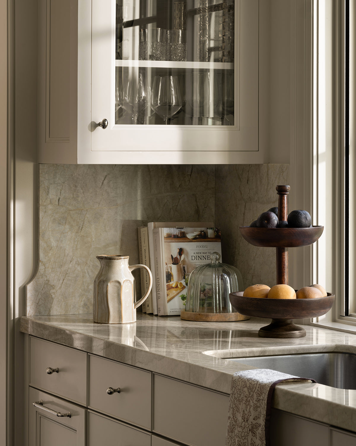 A glass cabinet above holds glassware, while the Marceline Cotton Tea Towel hangs from a drawer for charming decor, by Vendixs