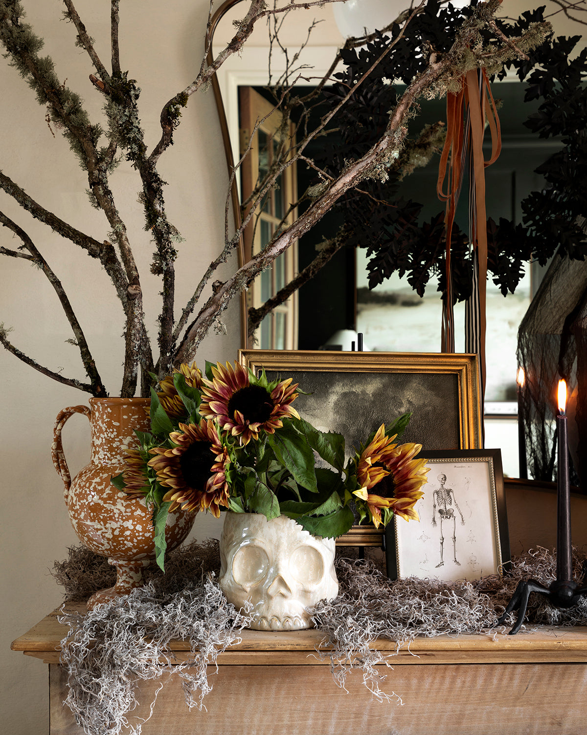 A wooden table with the Haunting Skull Vase filled with sunflowers, plus a branch-filled jug, framed art, black candles, and moss makes a bold rustic centerpiece—ideal Halloween décor, by Vendixs